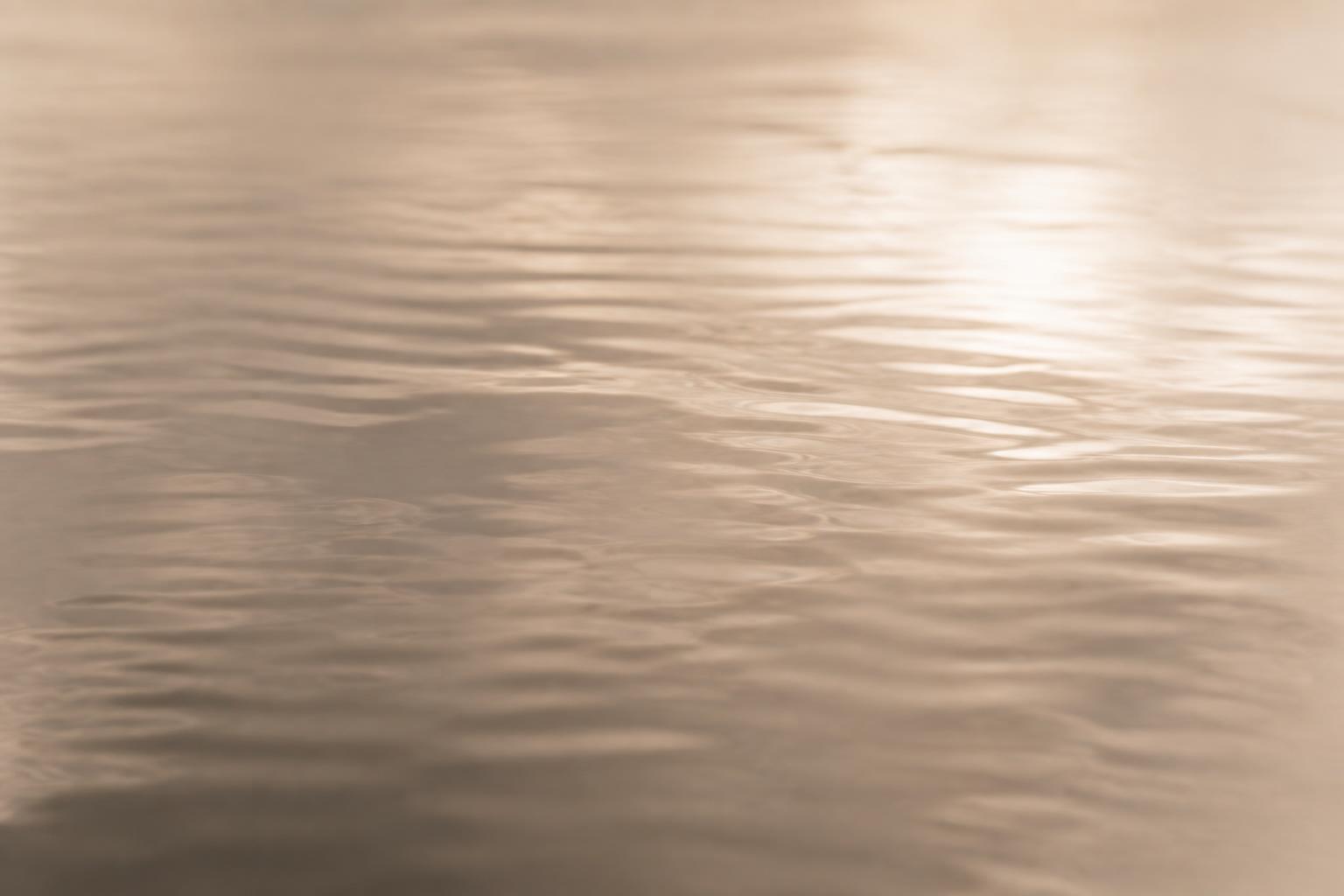 Soft warm water catching diffused light, gentle ripples in a restrained greige palette.